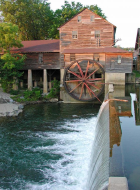 The historic Old Mill in Pigeon Forge, featuring a picturesque waterwheel and rustic mill structure. The mill is surrounded by trees, creating a tranquil, nostalgic atmosphere.

