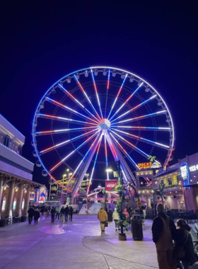 The Great Smoky Mountain Wheel at Pigeon Forge, a towering Ferris wheel with gondolas, set against a scenic mountain background. The illuminated wheel adds a lively touch to the evening sky.