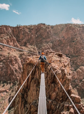 This image shows the Royal Gorge Bridge stretching across a deep canyon, with the Arkansas River flowing below and steep cliffs on either side.