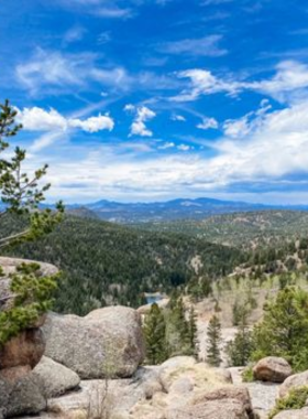 This image shows a scenic hiking trail at Mueller State Park, surrounded by trees and rolling hills, with bright sunshine filtering through the leaves.