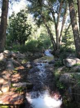 This image shows the beautiful Helen Hunt Falls in North Cheyenne Cañon Park, cascading down rocky cliffs into a tranquil pool surrounded by green trees.