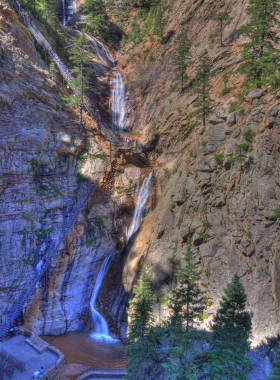 This image shows the cascading waterfalls of Seven Falls, with water tumbling down a steep canyon surrounded by tall cliffs and vibrant greenery.