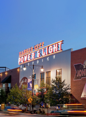 "This image shows the lively Power & Light District at night, with neon signs, bars, and people enjoying the energetic nightlife of Kansas City’s entertainment hub."