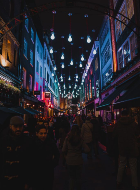  This image shows a vibrant Soho street at night, filled with neon lights, bars, and cultural diversity.