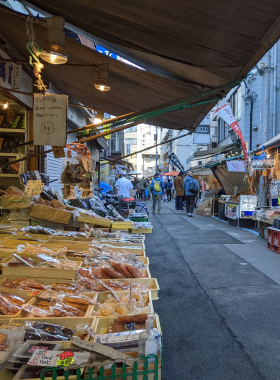 This image shows the vibrant Tsukiji Outer Market where visitors enjoy fresh sushi for breakfast. The market is bustling with people, vendors selling seafood, and colorful stalls offering sushi delicacies. The fresh seafood on display highlights the authenticity and variety of Tokyo’s seafood cuisine.