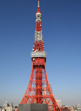  This image shows the stunning panoramic view of Tokyo from the top of Tokyo Tower. In the foreground, the tower’s red and white design stands tall against a clear sky, while the sprawling cityscape below stretches as far as the eye can see, offering a breathtaking perspective of Tokyo.