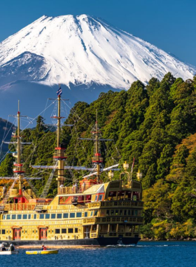 This image shows Mount Fuji in the distance, with clear skies and scenic landscapes surrounding the iconic peak. Visitors are seen enjoying a day trip to Mount Fuji, either hiking or sightseeing by the lakes, with breathtaking views of the mountain that are especially striking on clear days.