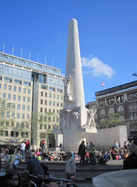 This image shows the lively Dam Square in Amsterdam, with crowds of visitors, the Royal Palace, and historical buildings surrounding the central area, creating a vibrant urban atmosphere.