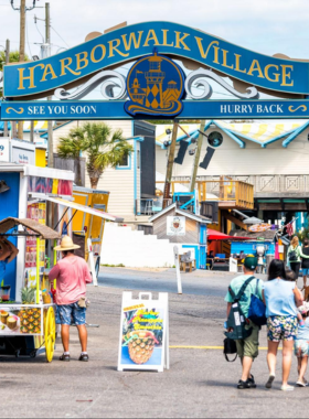 This image shows the vibrant HarborWalk Village, with a busy boardwalk lined with shops, eateries, and visitors enjoying activities by the marina.