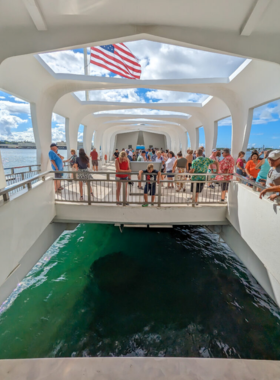 This image shows the USS Arizona Memorial at Pearl Harbor, a solemn site surrounded by clear blue water, with visitors paying their respects. The white structure stands as a tribute to those who lost their lives during the attack on December 7, 1941.