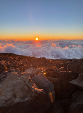 This image shows the vibrant colors of sunrise at Haleakala National Park, with layers of clouds below and the volcanic crater in view.