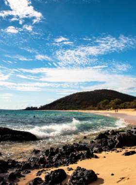 This image shows a vibrant sunset over Makena State Park, with the ocean reflecting warm hues and lava rock formations in the foreground.