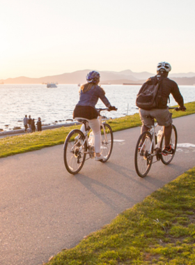 "This image shows cyclists enjoying a ride along False Creek in Vancouver, with stunning waterfront views of the city’s skyline and surrounding parks."