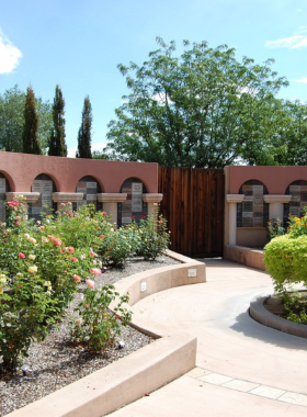 This image shows a vibrant flower display in the Albuquerque Botanic Garden, surrounded by lush greenery and walking paths.