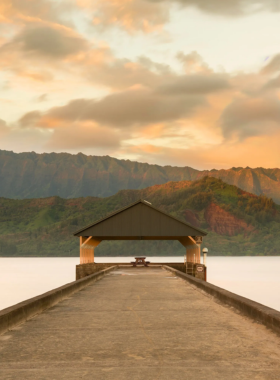 "This image shows Hanalei Bay on Kaua’i’s North Shore, with its stunning crescent-shaped beach, calm blue waters, and lush mountain backdrop perfect for water activities."