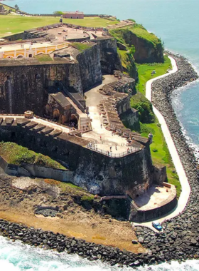 This image shows El Morro fortress standing majestically over the ocean, with stone walls and grassy fields in the foreground. The fort's historic architecture contrasts with the blue waves, reflecting Puerto Rico’s coastal defense history and scenic beauty.