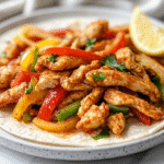 A top-down view of a vibrant plate of air-fried chicken fajitas on warm flour tortillas. The tortillas are filled with crispy chicken tenders, colorful red and green bell pepper strips, and caramelized onions. The plate is placed on a clean white marble countertop, showcasing a deliciously healthy meal ready to serve.