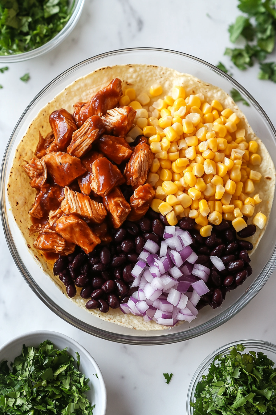 A clean top-down shot of tortilla chips topped with BBQ chicken, black beans, sweet corn, and chopped red onion. The ingredients are evenly distributed on a white baking sheet. Each colorful topping sits over crisp chips on a marble countertop, creating the perfect base layer before cheese is added and the nachos are baked.