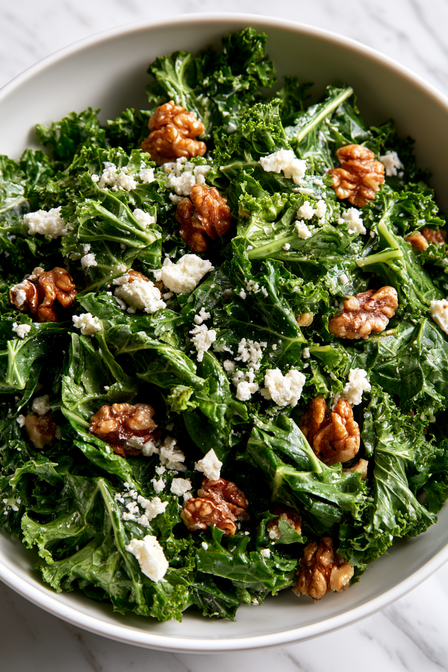 Pour the vinaigrette over the massaged kale and toss well to coat every leaf evenly. Sprinkle the toasted walnuts and crumbled feta cheese over the salad
