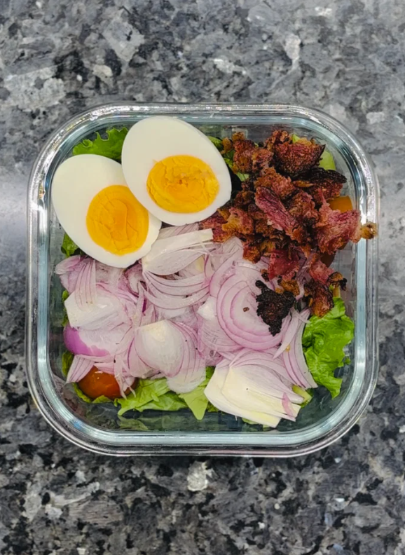 In a large bowl, layer greens, sliced cherry tomatoes, sliced onions, hard boiled eggs, and crumbled bacon.