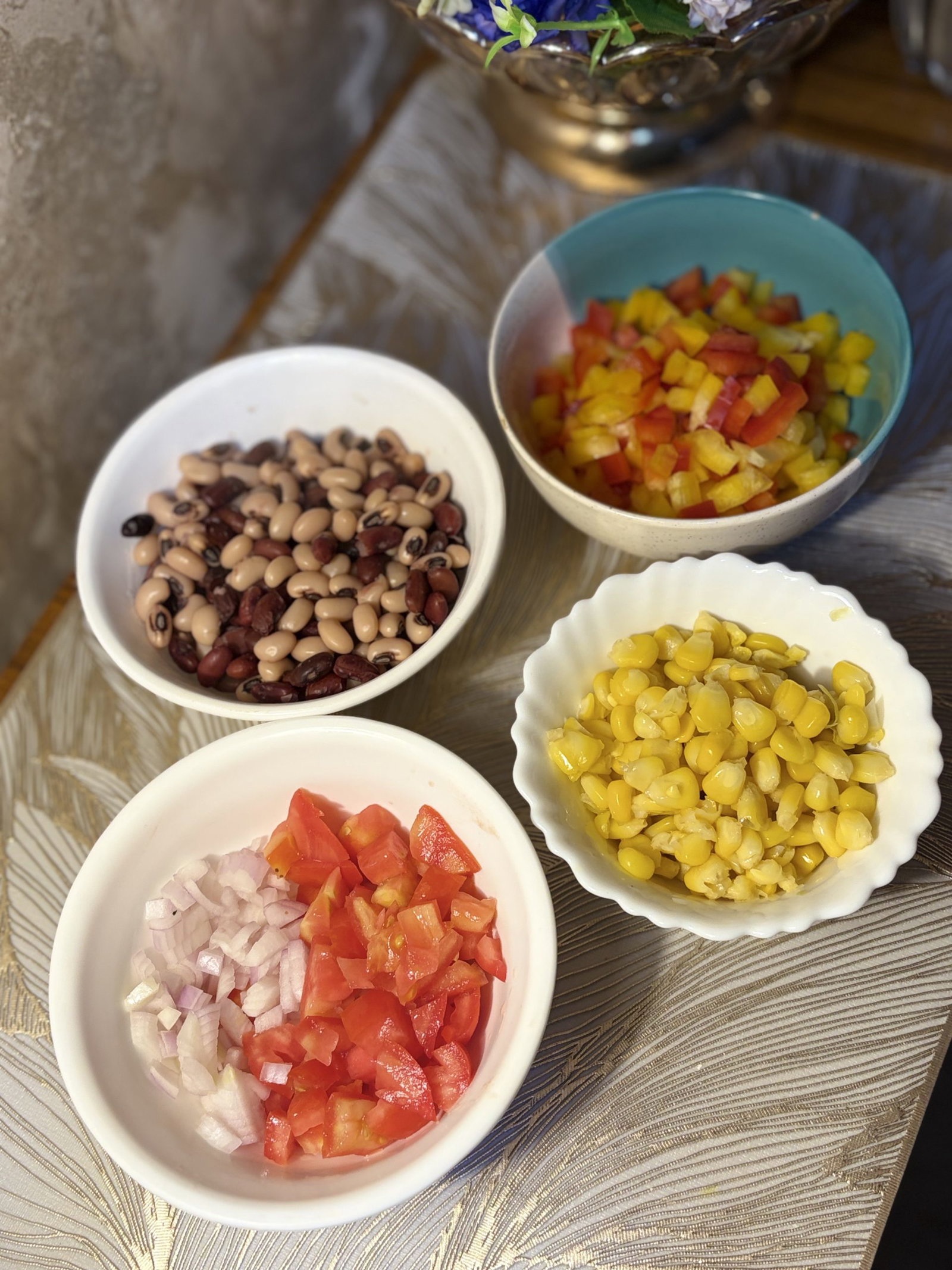 To the bowl of dressing, add diced bell peppers, roasted red peppers, jalapeños, drained black beans, black-eyed peas, corn, chopped tomato, and the rinsed onion