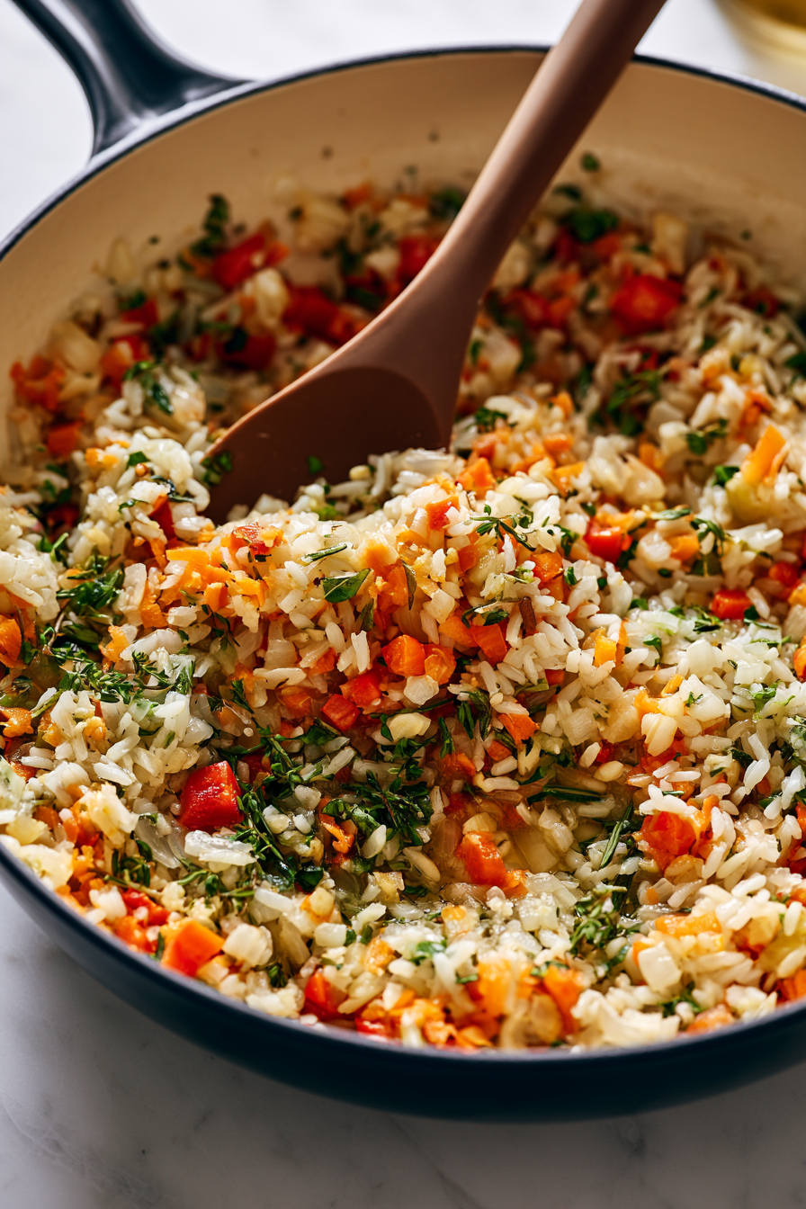Stir in the rice, carrot, bell pepper, garlic, thyme, rosemary, and basil. Cook for 2 to 3 minutes until the rice is lightly toasted